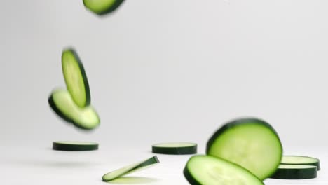 fresh green cucumber coins falling onto table, bouncing, flipping and settling into a pile in slow motion