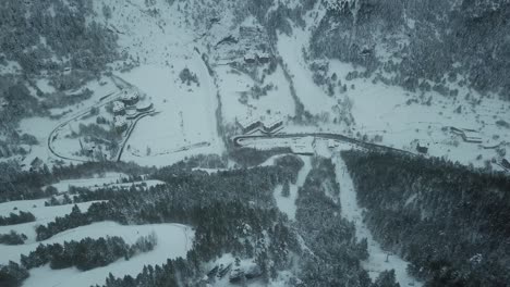 drone tilt up to down, unveiling some buildings at the base of a snow mountain, covered by trees
