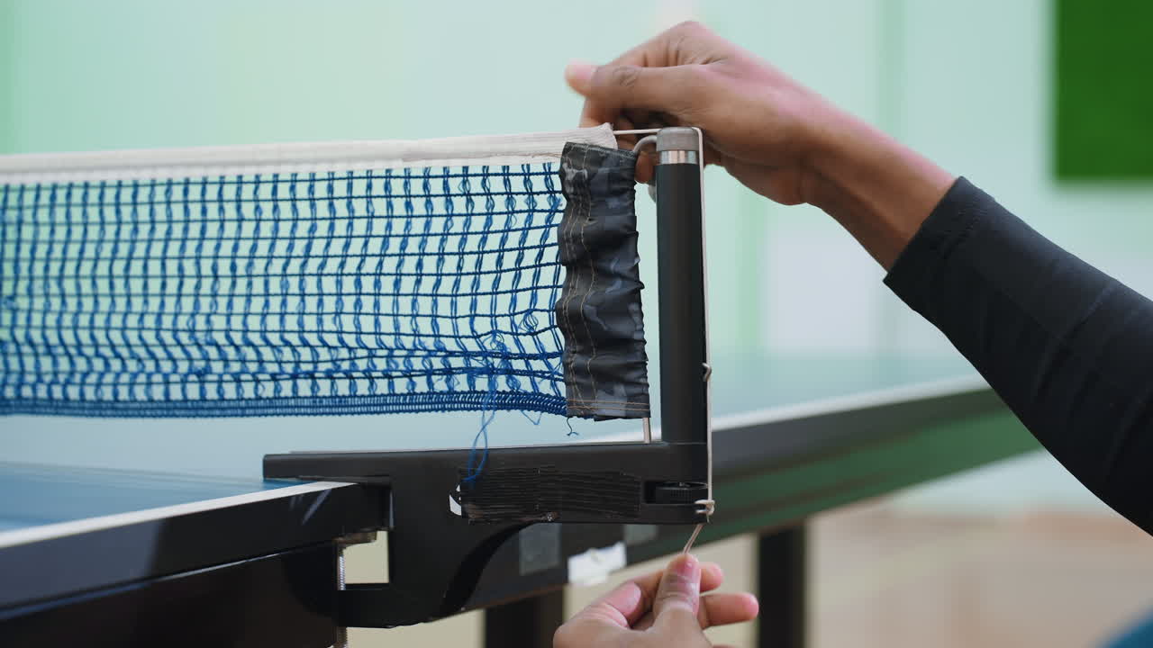 Close up of athlete tightening table tennis net indoors, focusing on proper setup and accuracy before game, showing discipline, precision, and readiness for competitive sports activity