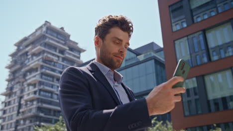 un hombre de negocios exitoso enviando mensajes de texto en su teléfono inteligente caminando por la calle de cerca.