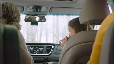 vista trasera de tres amigos bebiendo té caliente mientras están sentados en el auto en un día de invierno