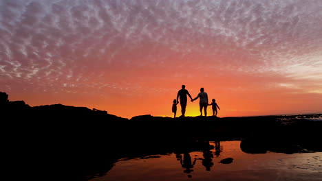 familia en la costa rocosa disfruta del atardecer de fuego