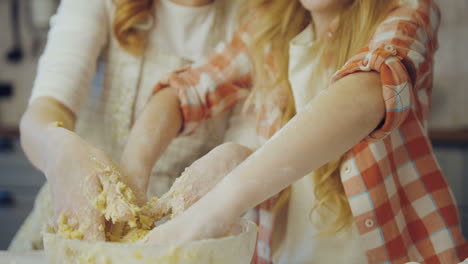 Close up of the happy smiled mother and daughter kneading a daugh together in the big glass bowl in the kitchen. Portrait. Indoor