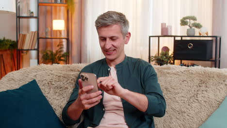 Smiling man celebrates smartphone victory with clenched fist joyfully reacting to good result