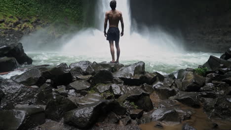 Schwenken-Nach-Oben,-Um-Einen-Mann-Zu-Enthüllen,-Der-Zu-Einem-Donnernden-Dschungelwasserfall-Aufschaut,-Zeitlupe