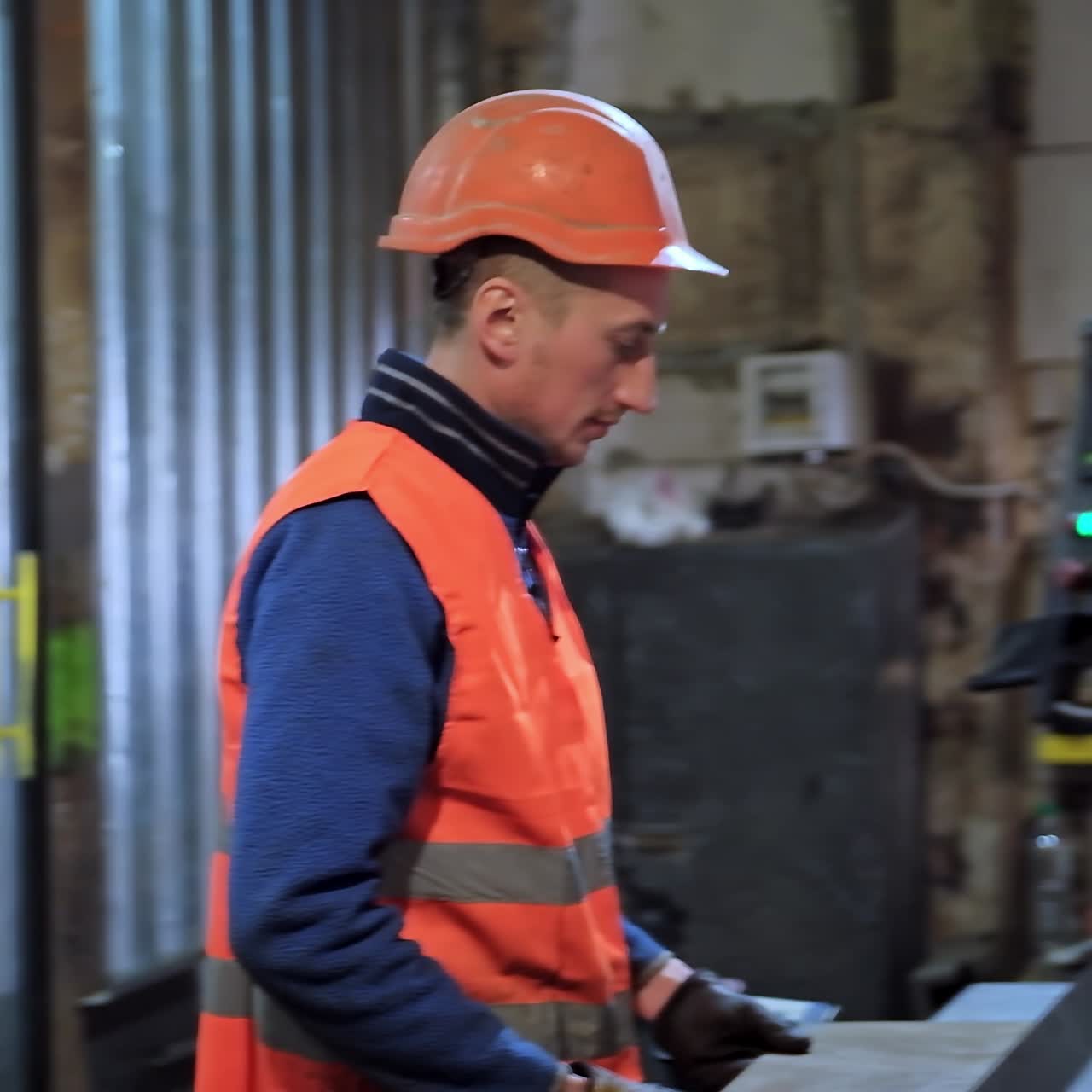 Manufacturing indoors. Male worker in uniform and hard hat working on the industrial materials background inside the plant. Slow motion.