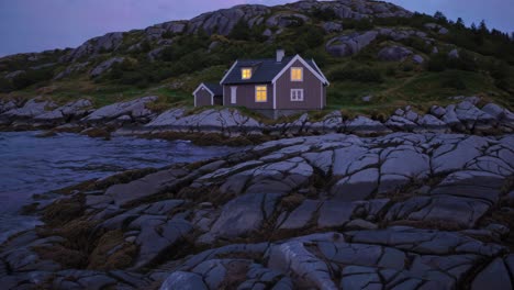 warm lights glowing from windows of a solitary house on a rocky norwegian coastline, creating a tranquil scene as twilight envelops the serene nordic landscape