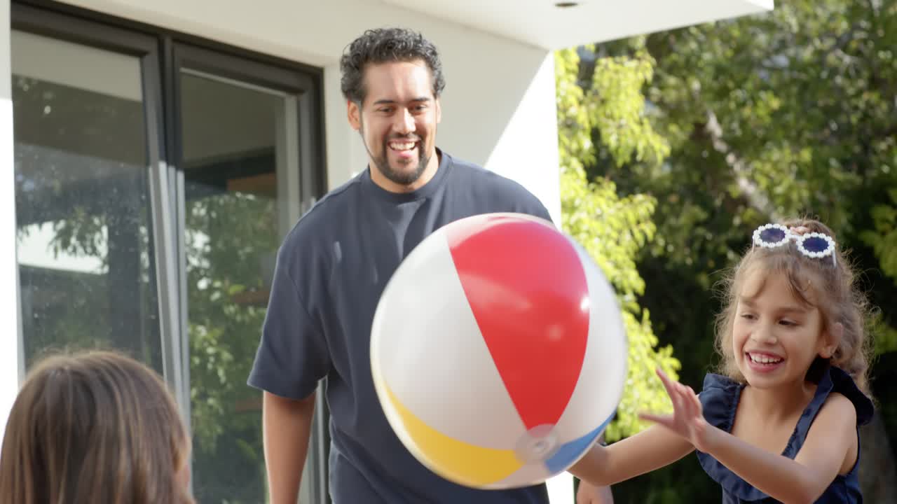 Familjebarn sträcker sig efter färgglad strandboll när en vuxen räcker över den, en man kastar den på uteplatsen och leker