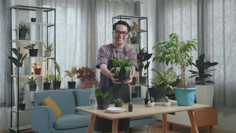 smiling asian man holding and showing the plant to camera at home