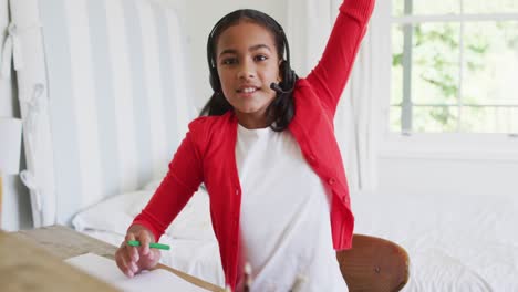 Mixed-race-girl-at-home-in-online-school-class,-using-headset-raising-hand