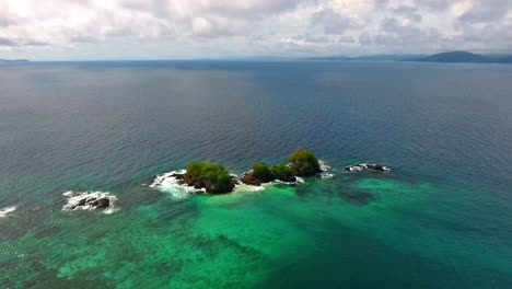 rising aerial view over small coral islands with clear water and surrounding waves