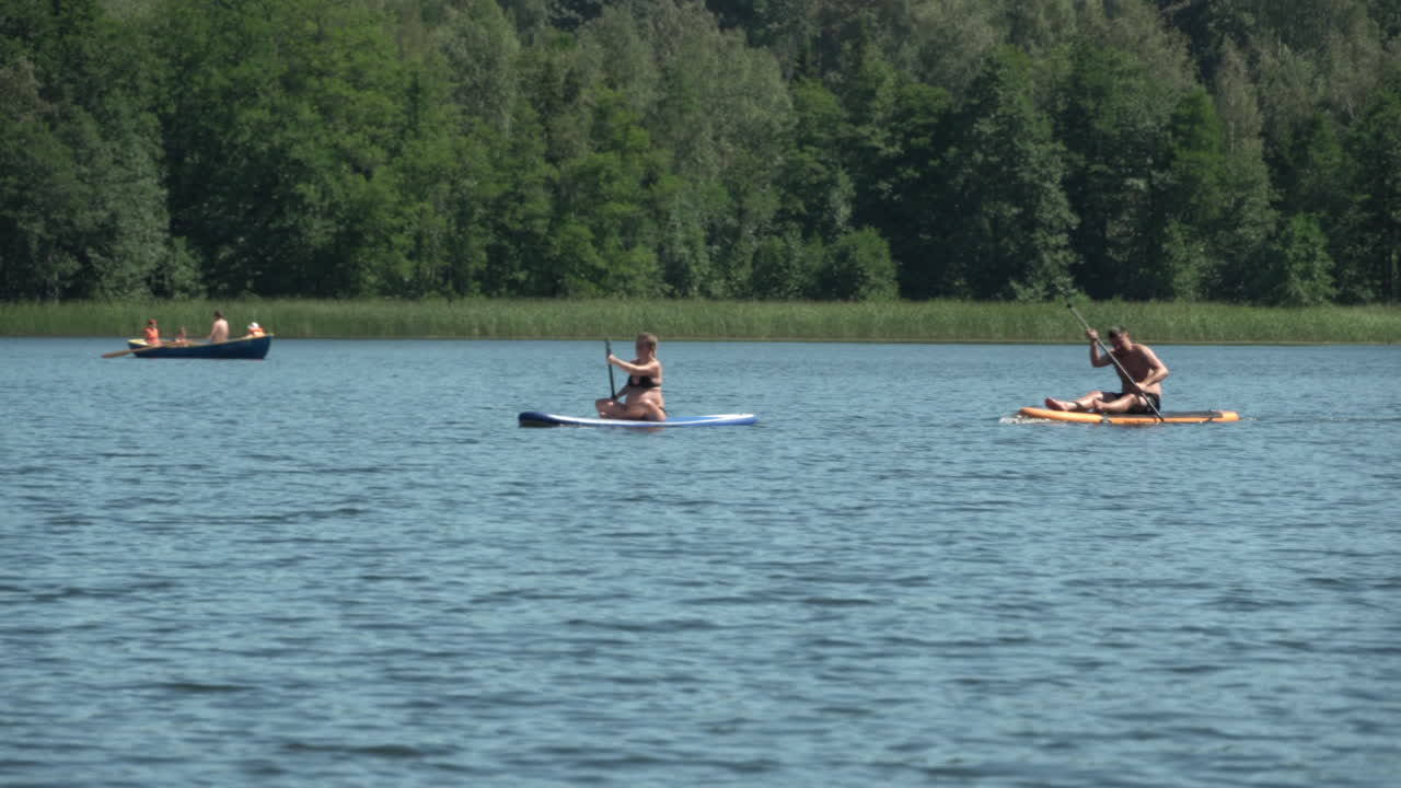 Men  and woman with sup boards at lake. Forest  background. Hot sunny summer day.