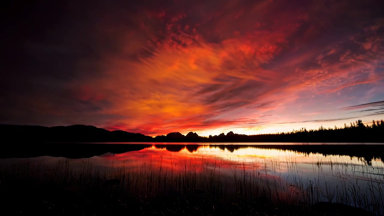 Zeitraffer von leuchtenden Sonnenuntergangsfarben, die sich in einem ruhigen Bergsee spiegeln
