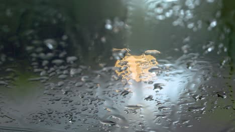 defocused headlights drive by a parked car with a rain-streaked windshield