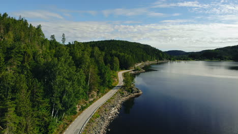 Aerial-view-of-empty-road-winding-along-blue-lake-next-to-green-forest