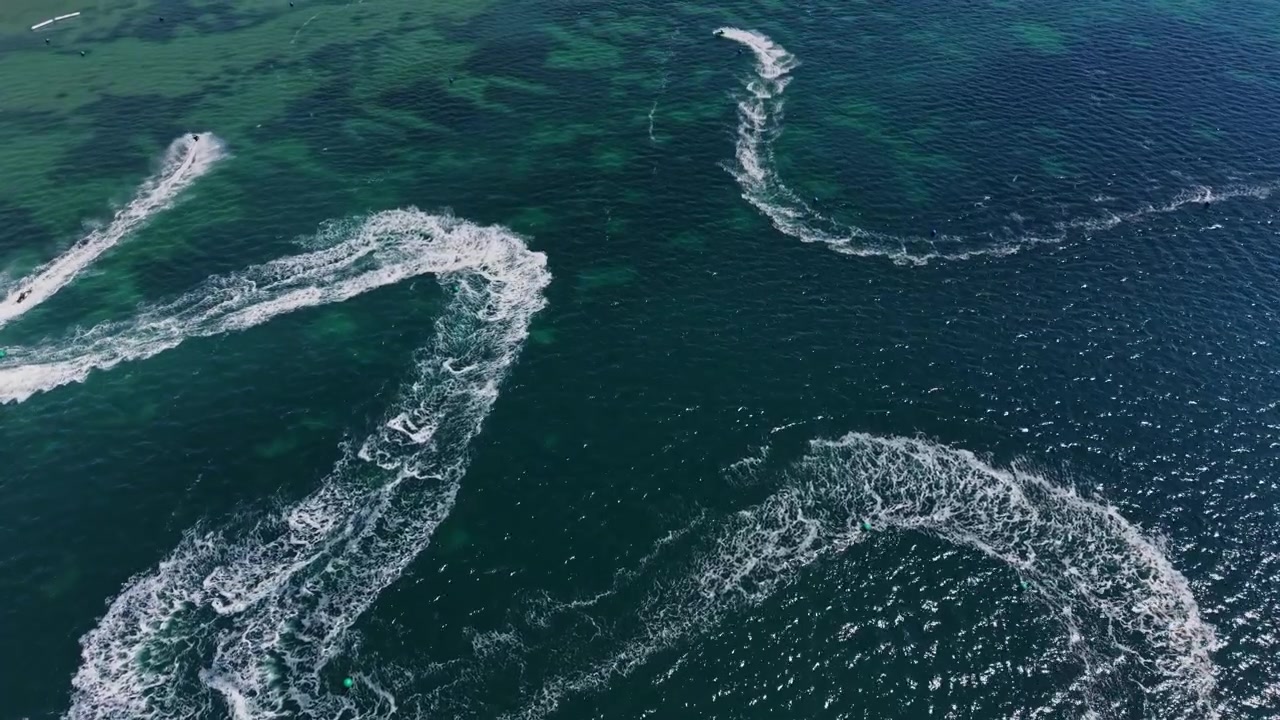 Watercrafts move in curves on clear water during a sunny day at the shore