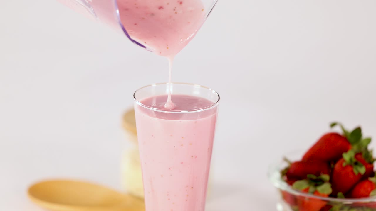 Creamy strawberry smoothie pours into glass, bright lighting, fresh berries, clean white background, static shot