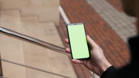 green screen, close-up view of a person holding a smartphone swiping pages on mockup outdoor