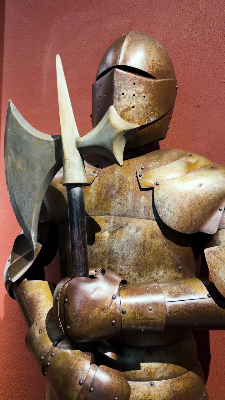 Armure médiévale en acier tenant une grande hache contre un mur rouge chaud dans une exposition intérieure, verticale