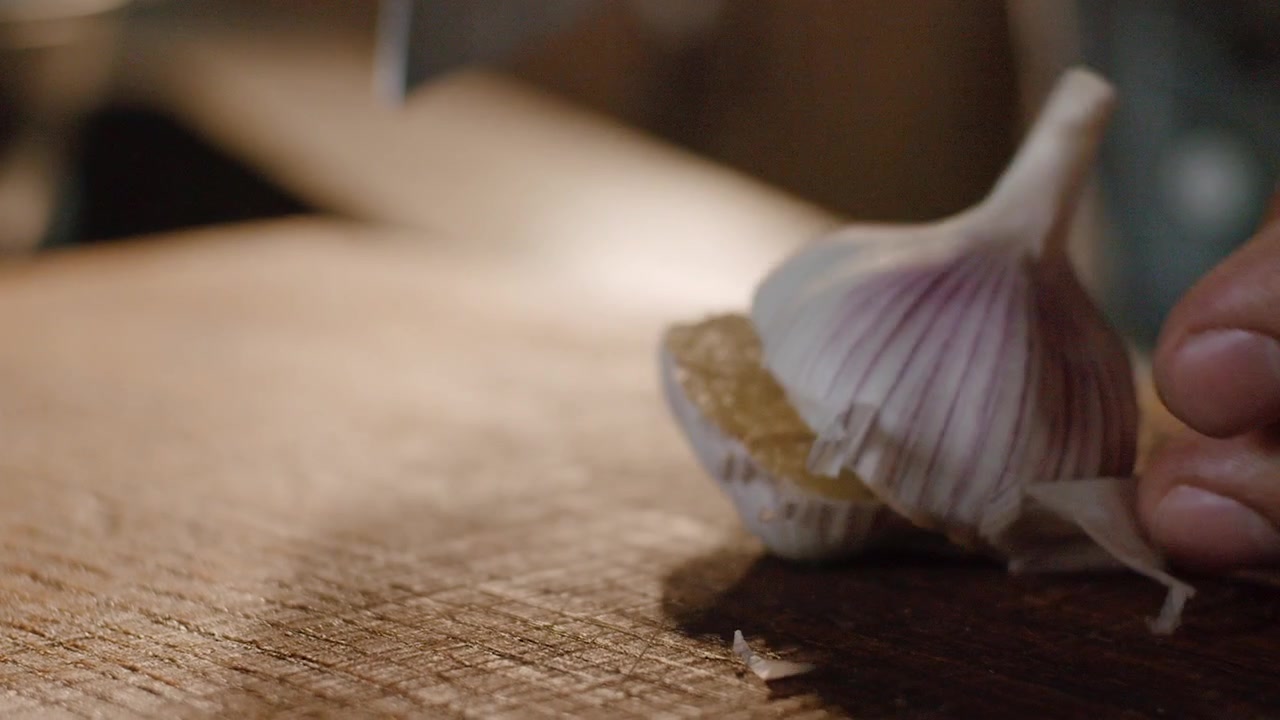 Taglio di un bulbo d'aglio intero a metà su un tagliere di legno, mani in primo piano