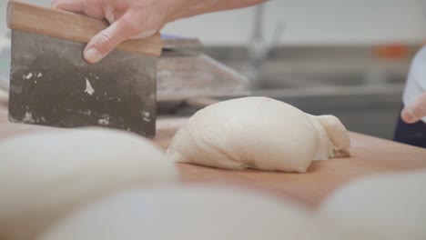 bakery scene of baker using dough scraper to form a bread loaf on a table