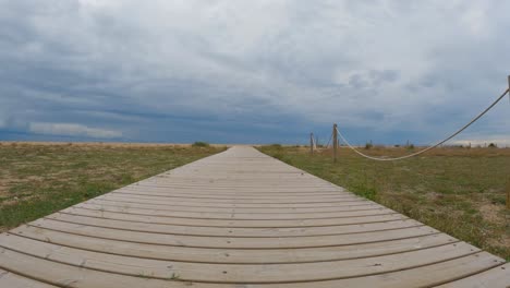 wooden bridge over the sand direction to the beach walking in slow motion gimbal drone cloudy stormy day