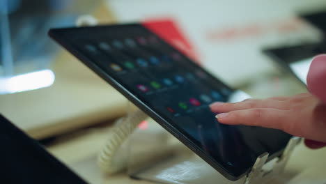 hand in pink dress interacting with a tablet on display stand in a bright store, using the screen to operate the device, tablet positioned on sleek stand with blurred movement in background