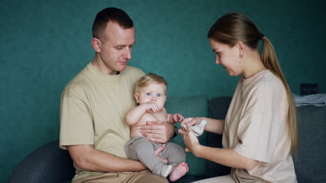 mom puts on socks on her infant child held by the dad. parents take care of their cute baby.
