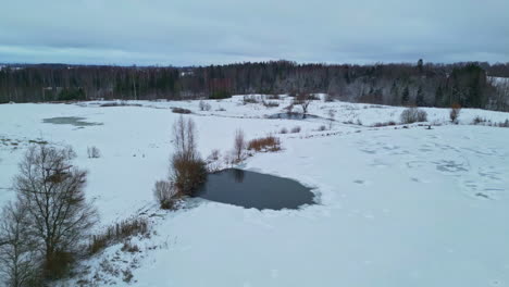 Aerial-view-of-pond-between-frozen-winter-wonderland-landscape-of-Latvia