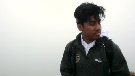 man checks his watch while standing outside in the fog and wind