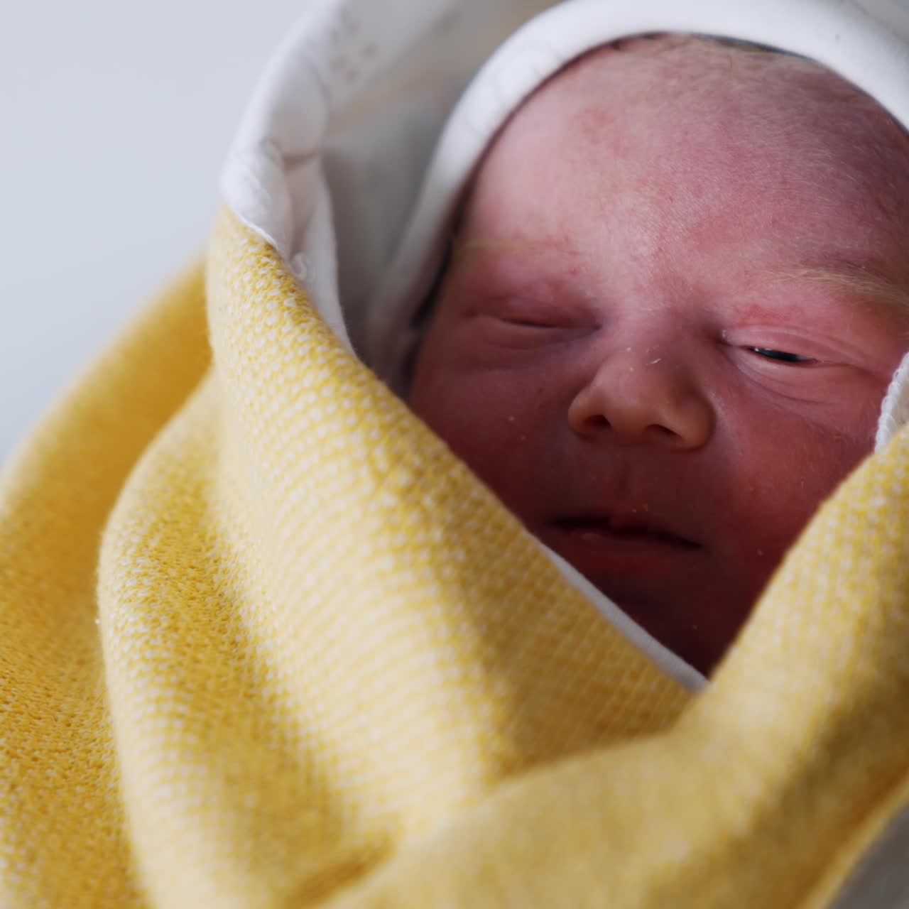 Face of a Caucasian newborn peeping out from the layer of wraps. Few hours-old baby in parent's hands. Close up