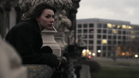 young woman in a black coat standing on a terrace enjoying the view and smoke