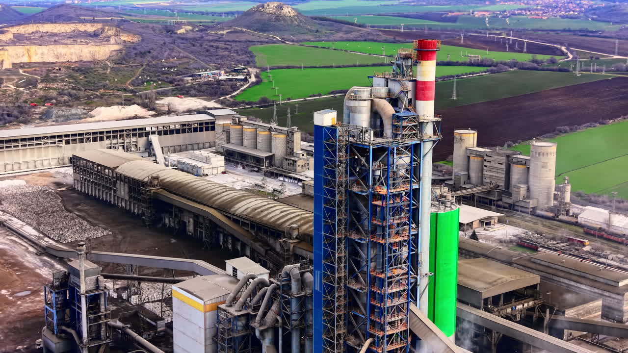 Aerial perspective of industrial buildings, blue and green silos, and complex piping systems at a factory. Detailed aerial view of heavy industry manufacturing facility