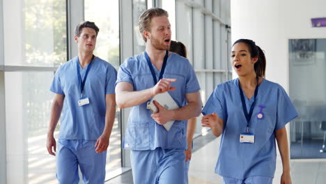 medical interns wearing scrubs walk towards camera in busy hospital