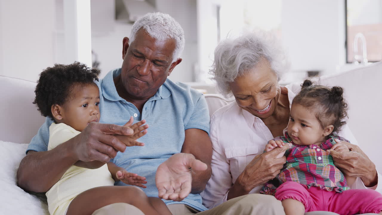 Grandparents Sitting On Sofa At Home Playing Game With Baby Granddaughters
