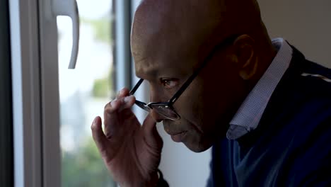 un hombre negro pensativo siendo pensativo e investigador mientras se quita las gafas y mira por una ventana