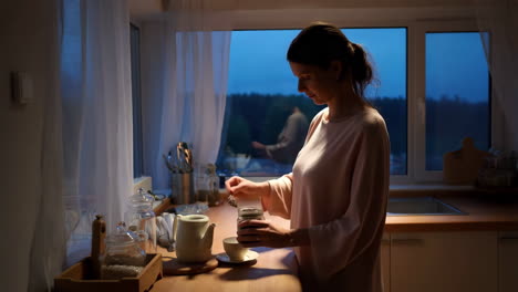woman preparing tea in her kitchen at dusk