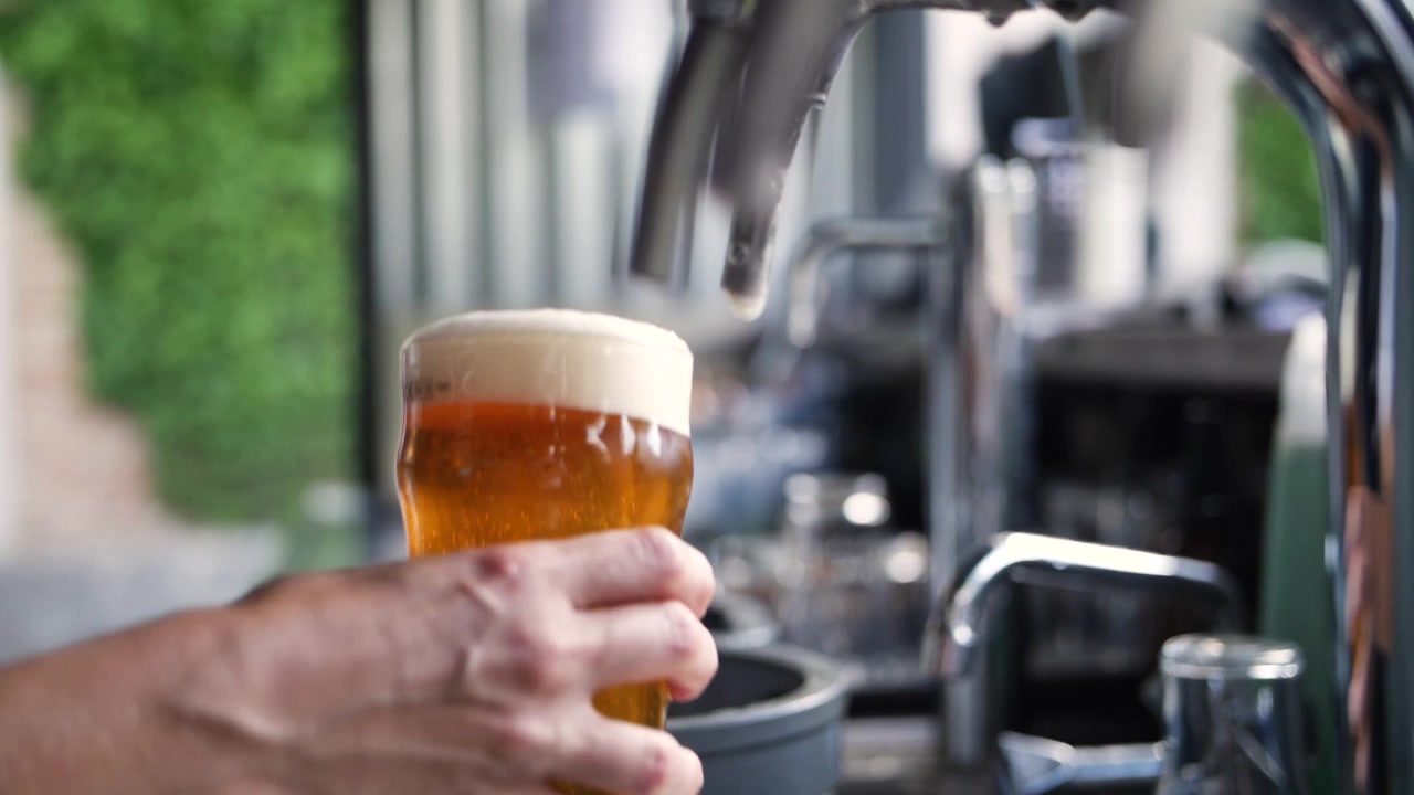 Bartender häller upp en pint gyllene öl på en trädgårdsfest i superslowmotion