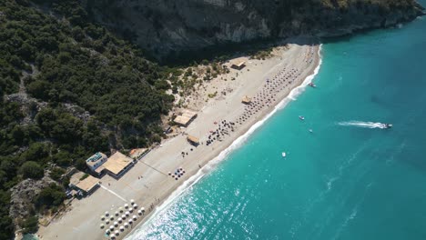 Vista-De-Pájaro-En-ángulo-Alto-Sobre-La-Playa-De-Arena-Blanca-En-La-Riviera-Albanesa,-El-Barco-Sale-Al-Mar