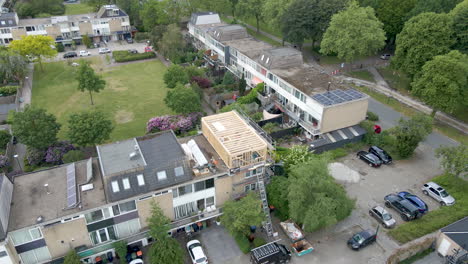 aerial overview of wooden frame of roof structure under construction in a busy suburban neighborhood - drone flying backwards