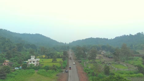 Drone-shot-along-busy-rural-Indian-village-road-farming-land-on-either-side