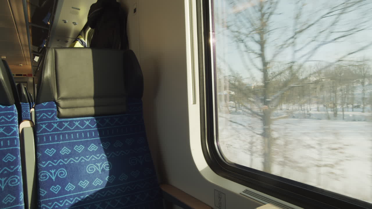 Posto finestrino vuoto su un treno, con paesaggio invernale bianco e nevoso che scorre all'esterno.