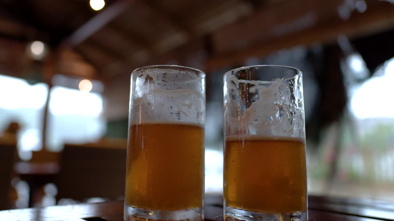 Primo piano di due bicchieri di birra su un tavolo di legno con l'illuminazione sfocata dello sfondo di un ristorante.