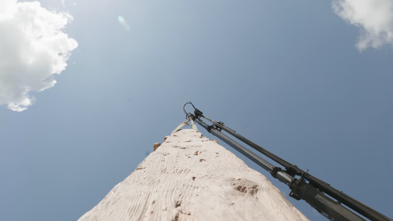 Wooden plank carried by crane jib against sky, bottom up, hanging log POV