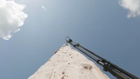 wooden plank carried by crane jib against sky, bottom up, hanging log pov