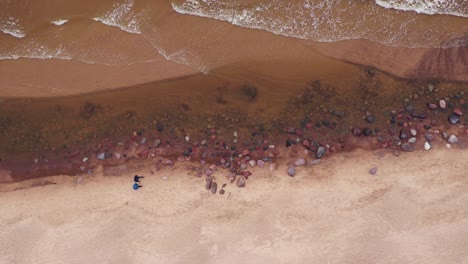 Unknown-Couple-walks-on-sandy-beach-with-stones-and-waves-hit-coast