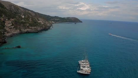 Drone-shots-of-5-yachts-anchored-next-to-Island-on-beautiful-blue-water-on-a-cloudy-day