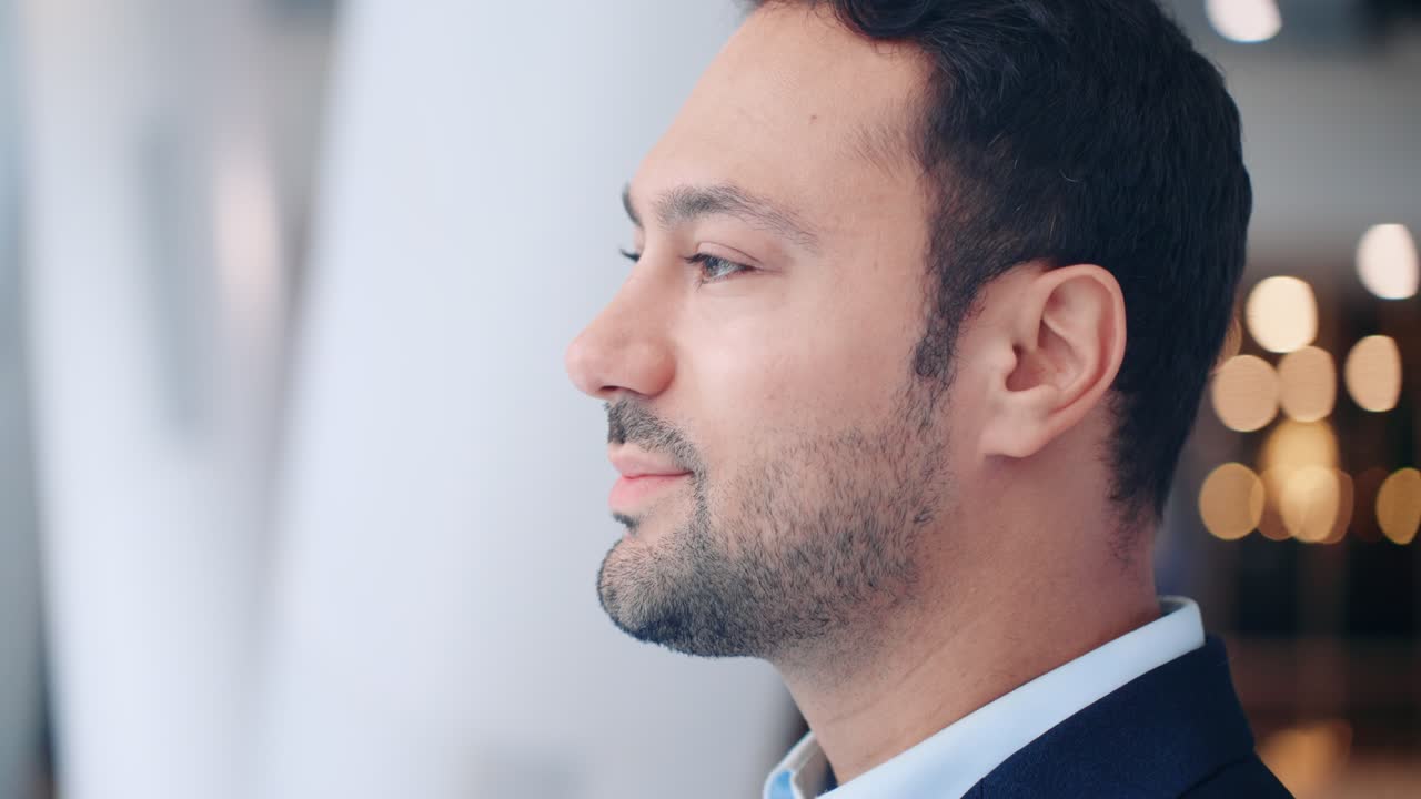 Primo piano di un uomo d'affari europeo pensieroso in giacca e cravatta, con un sorriso accennato, in piedi in un ambiente interno con un'espressione positiva e riflessiva