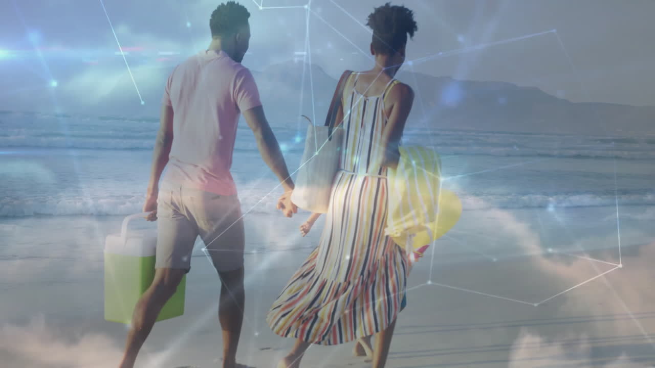 Couple walking along beach shoreline showing technology network overlay with cooler and sand bucket