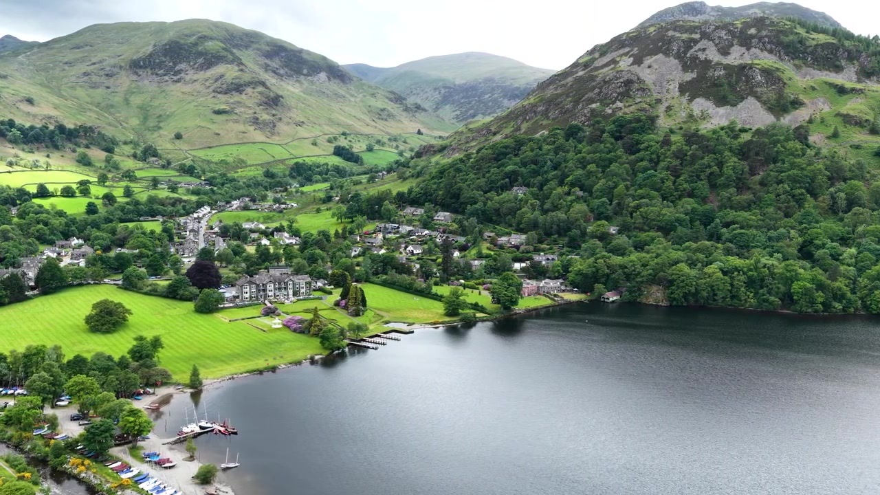 Splendide riprese con drone che sorvolano Glenridding e le rive di Ullswater nel Lake District. Panoramiche aeree del villaggio, delle colline circostanti, della campagna e delle acque tranquille.